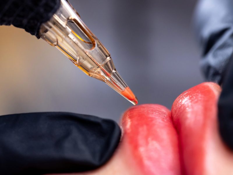 Macro photo of process of applying permanent makeup tattoo of red on lips woman.