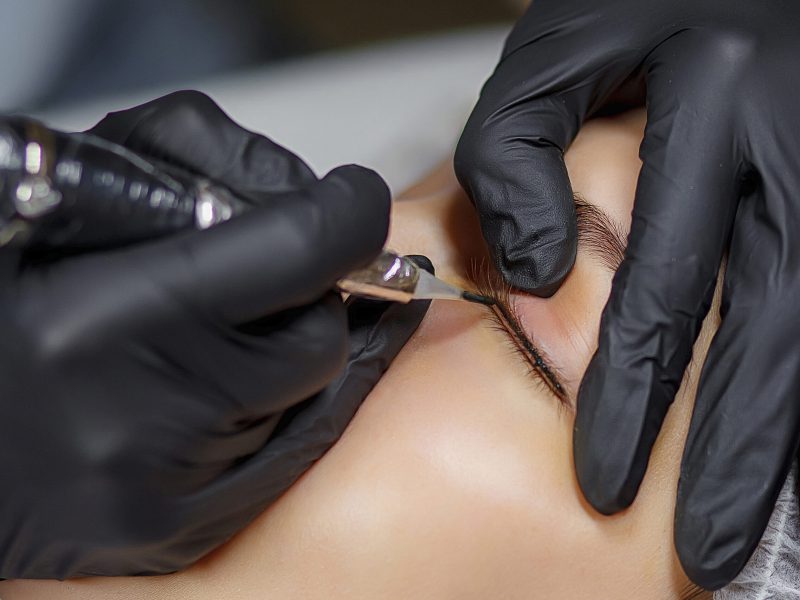 Permanent make up eyeliner procedure, applying on young girl. Close-up. Young beautiful woman making permanent makeup in cosmetology salon. Young girl applying permanent eyeliner in beauty studio